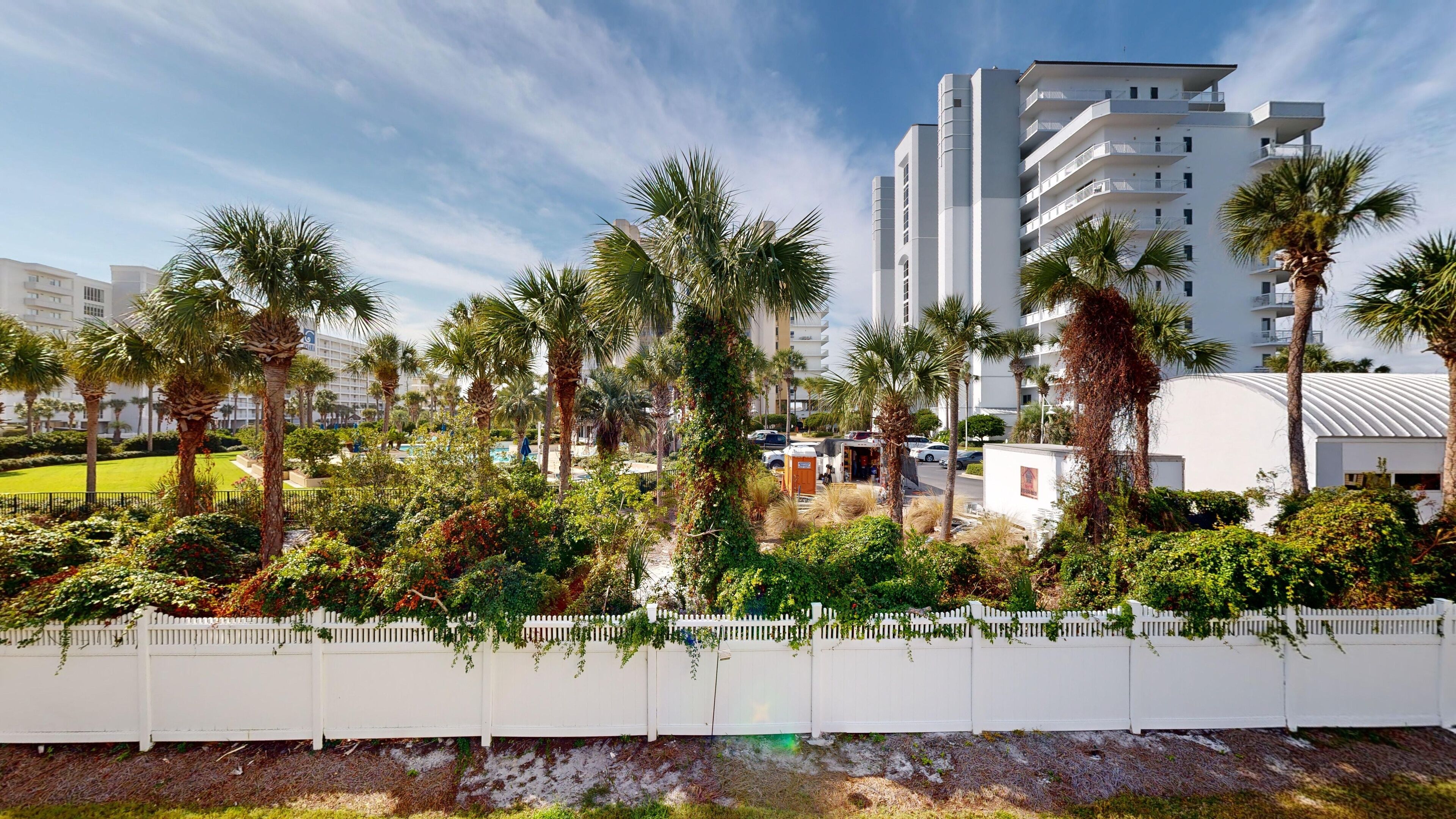 A hotel with a white fence, palm trees, and a pool area.