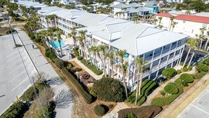 A multi-story hotel with a rooftop pool, surrounded by palm trees and a parking lot. - Grand Caribbean East 101 2 Bedroom Condo (Destin)