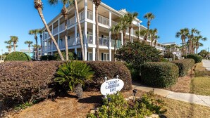 A multi-story hotel with balconies, surrounded by palm trees and well-maintained hedges. - Grand Caribbean East 101 2 Bedroom Condo (Destin)