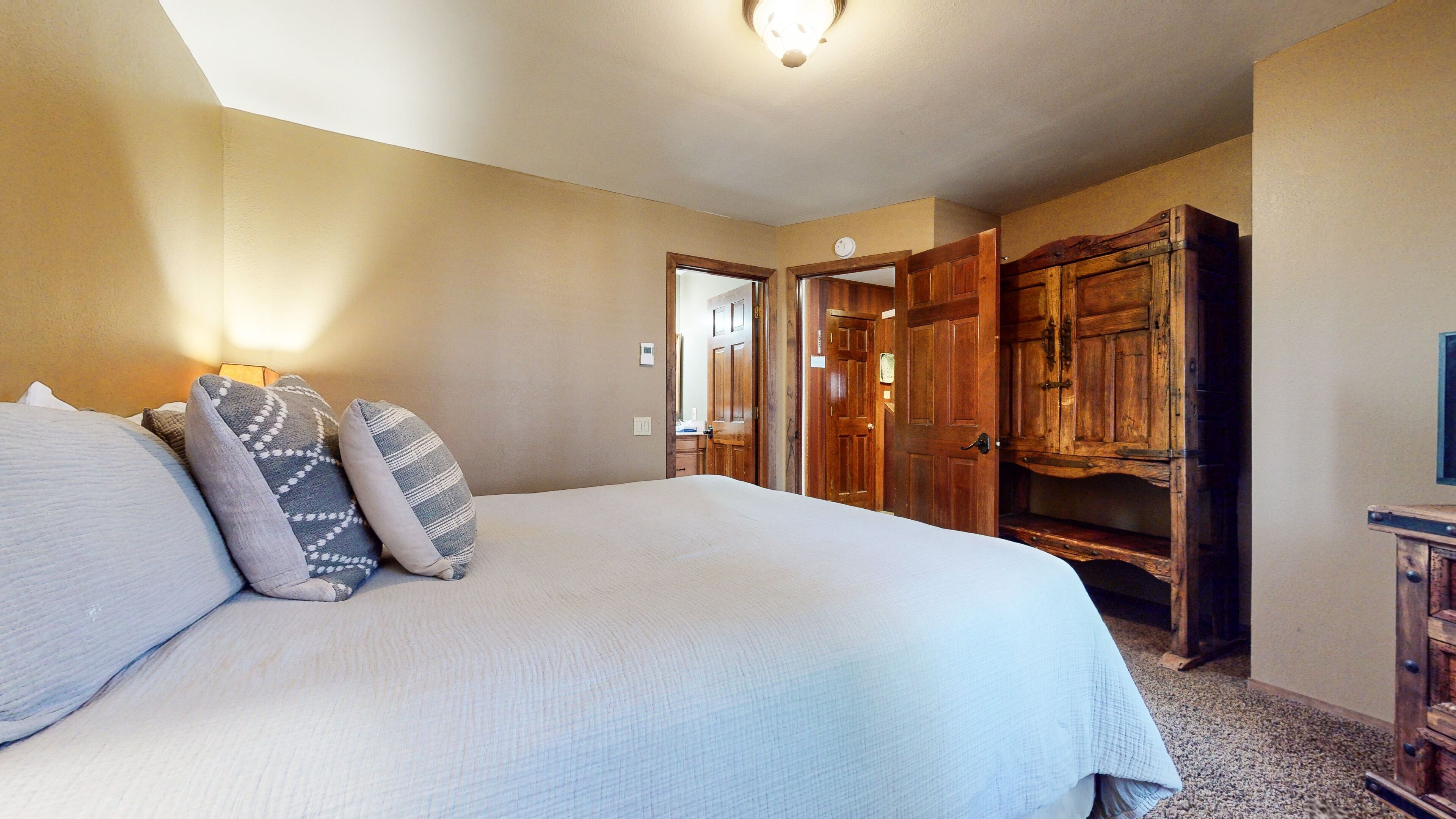 A bedroom with a large bed, a wooden wardrobe, and a door leading to another room.