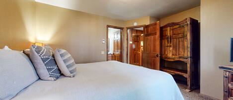 A bedroom with a large bed, a wooden wardrobe, and a door leading to another room.