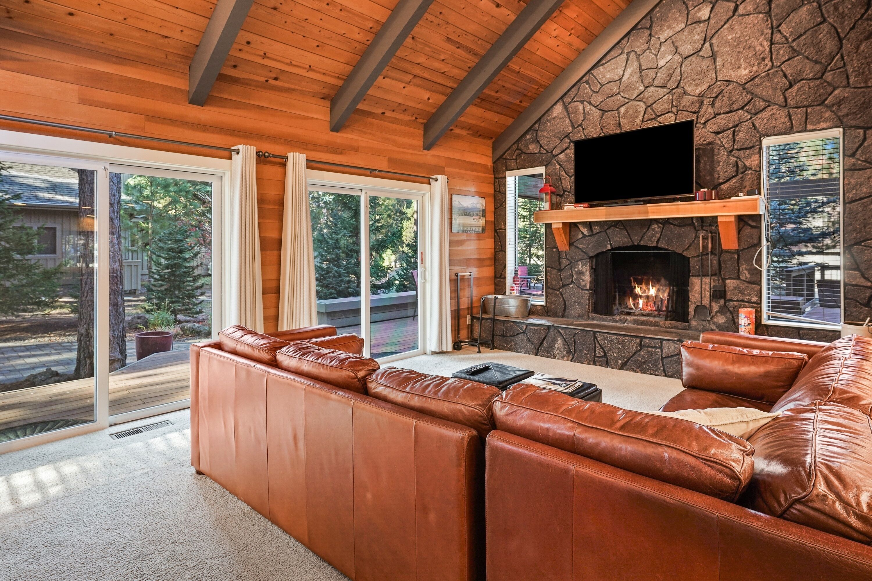 A cozy living room with a stone fireplace, leather sofa, and a flat-screen TV mounted above it.