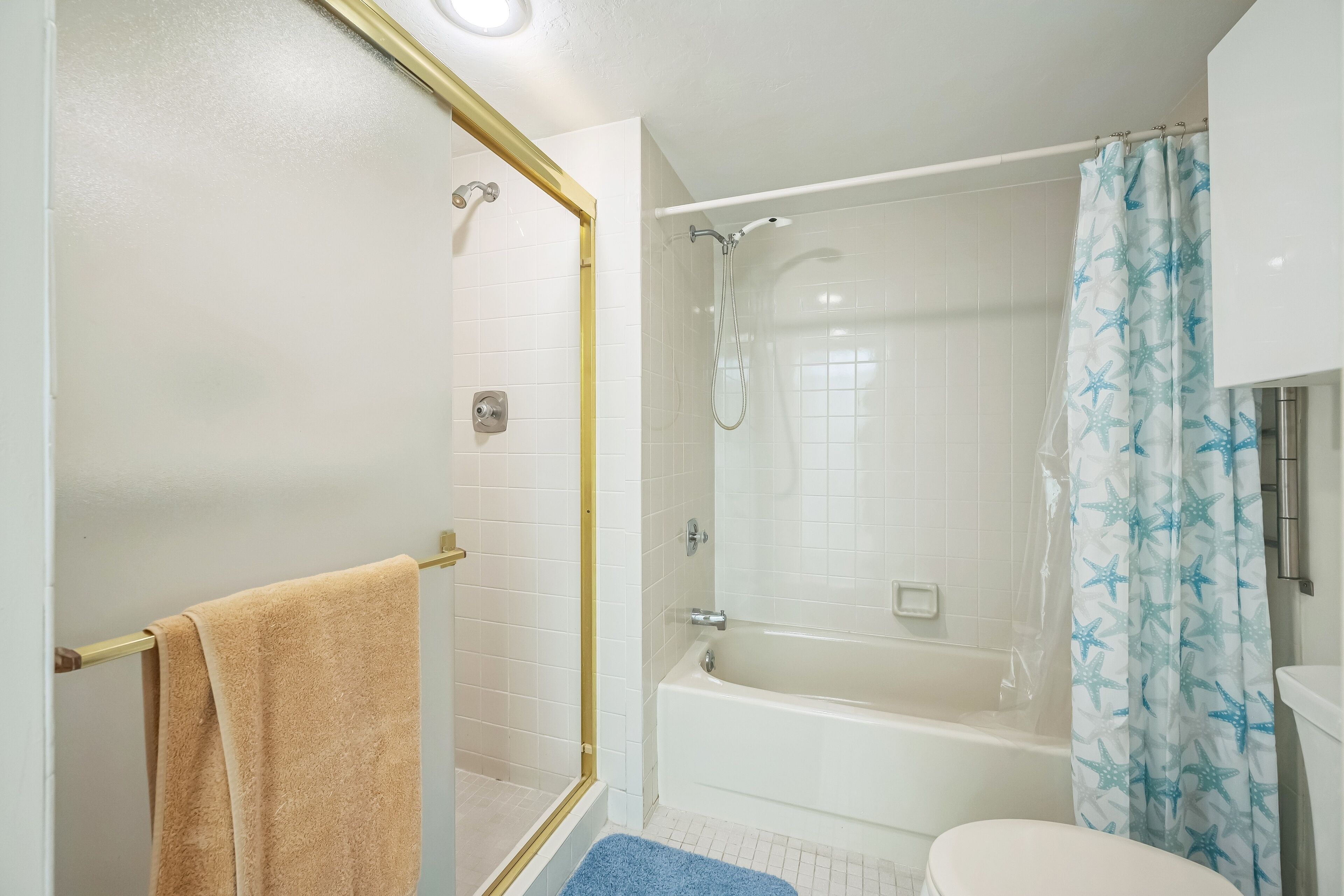 A bathroom with a shower, bathtub, toilet, and a towel rack.