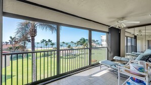A balcony with a view of the ocean, palm trees, and a pool area with lounge chairs. - Gulf-view Condo With Resort-style Amenities 2 Bedroom Condo (Marco Island)
