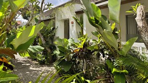 A building with a tiled roof and a white facade, surrounded by lush tropical plants. - Lubdhaka Canggu (Canggu)