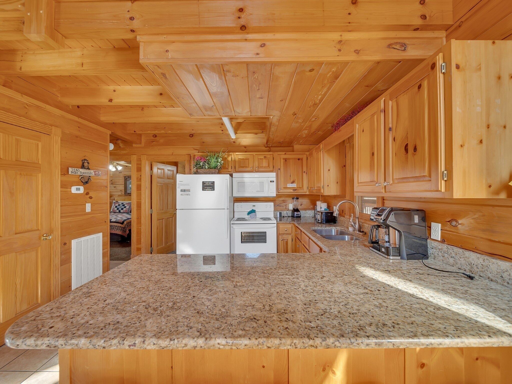 A wooden cabin interior with a kitchen featuring granite countertops, a refrigerator, a stove, and a sink.