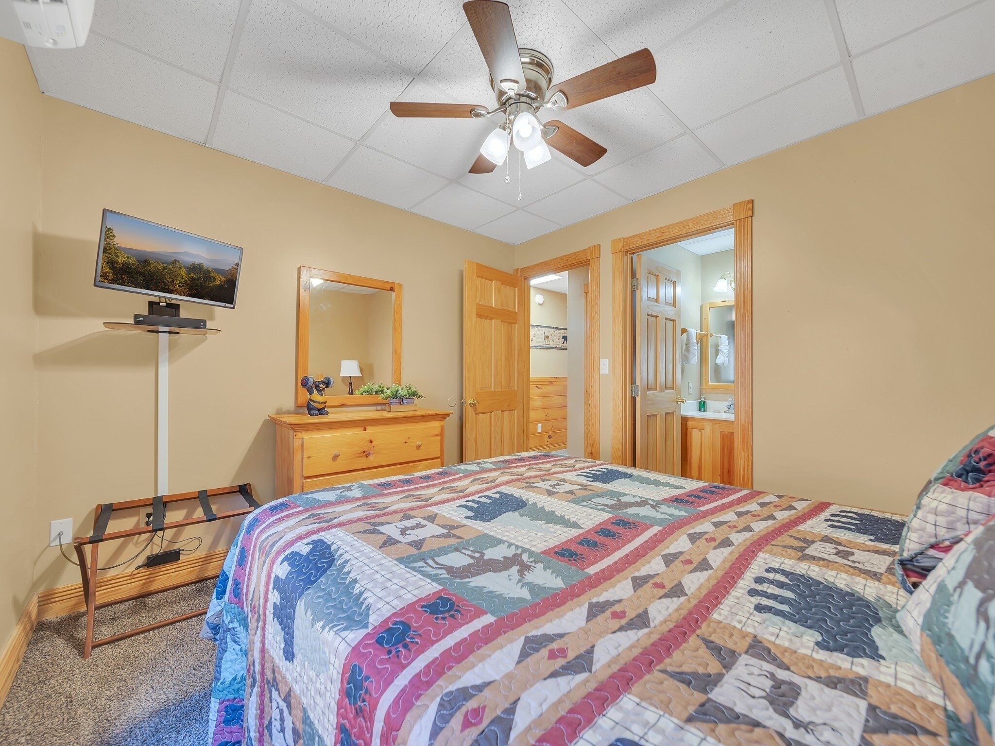 A bedroom with a bed, a dresser, a mirror, a ceiling fan, and a television.