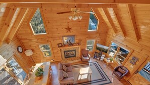 Interior acogedor de una cabaña con comedor, asientos, chimenea y ventanas amplias con vistas al exterior.