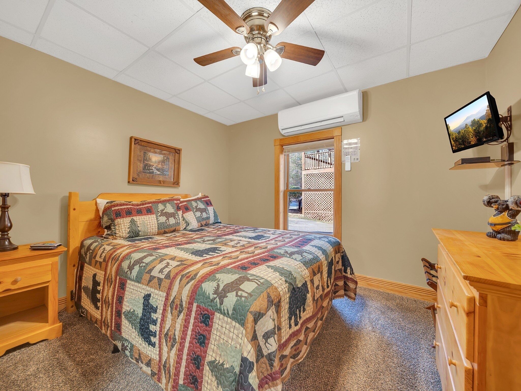 A bedroom with a bed, a ceiling fan, an air conditioning unit, a television, and a dresser.