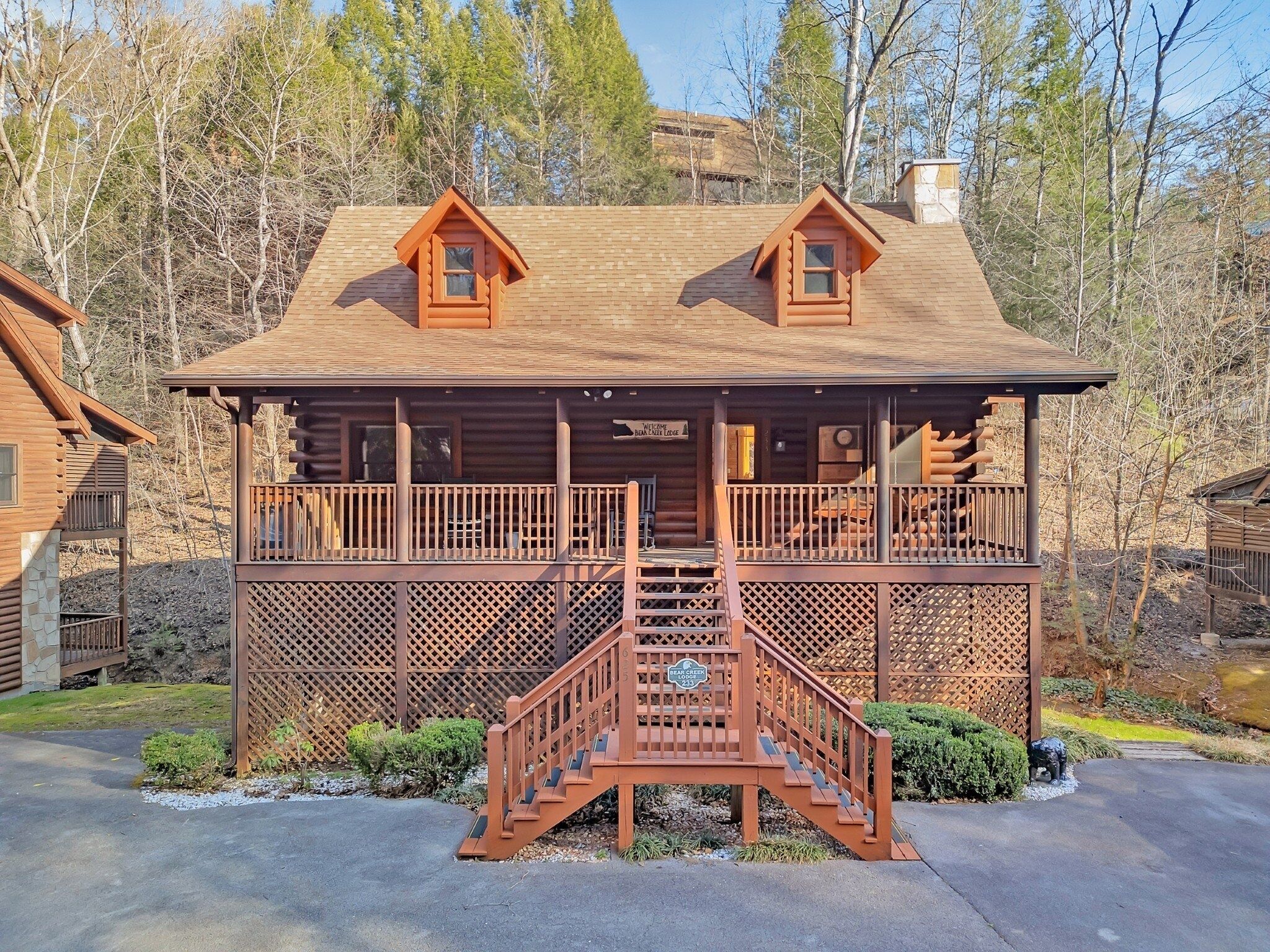 A log cabin with a porch, a staircase, and a sign that reads "Welcome Bean Belly Lodge".