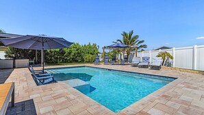 A rectangular swimming pool with a tiled deck, surrounded by lounge chairs and umbrellas. - Soak Up The Sun - Saltwater Pool, Spacious Fenced-in Backyard, 3 Bedroom Home (Cape Coral)
