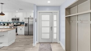 A modern kitchen with white cabinets, stainless steel appliances, and a grey door. - Soak Up The Sun - Saltwater Pool, Spacious Fenced-in Backyard, 3 Bedroom Home (Cape Coral)