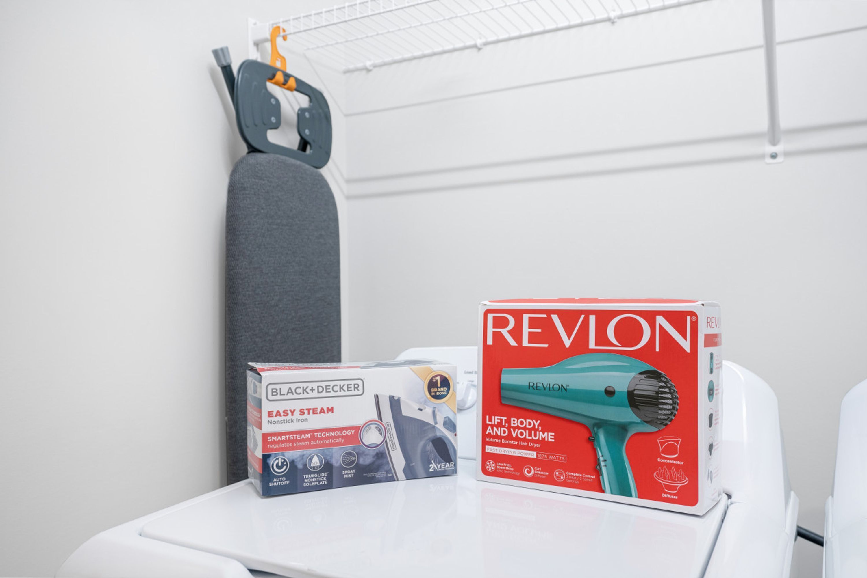 A bathroom with a white sink, a grey towel, a black and decker steam iron, and a reylon hair dryer on a white countertop.