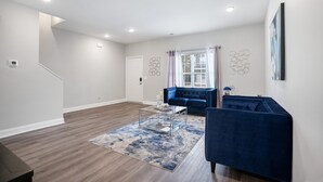 Un salon spacieux avec un canapé bleu, une table basse et une grande fenêtre agrémentée de rideaux.