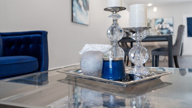 Un salon moderne avec une table basse en verre, un canapé bleu et des objets décoratifs, notamment des bougies et un vase.