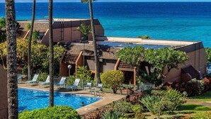 A pool area with lounge chairs, a view of the ocean, and solar panels on the roof.