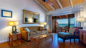 A spacious living area with a wooden floor, a sofa, a glass coffee table, a ceiling fan, and a large mirror.