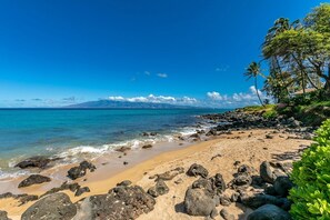 A beach with clear blue water, rocky shoreline, and a mountain in the distance. - Kuleana Resort 205 2 Bedroom Condo (Lahaina)