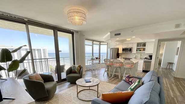 A spacious living area with a sofa, chairs, a coffee table, and a view of the ocean through large windows. - 1703 Brighton, Newly Remodeled Condo With Full Access! 3 Bedroom Condo (Myrtle Beach)
