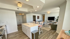 A modern kitchen with white cabinets, a central island, and a dining area with white chairs. - 1703 Brighton, Newly Remodeled Condo With Full Access! 3 Bedroom Condo (Myrtle Beach)