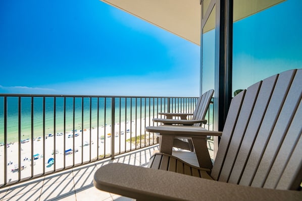 A balcony with a view of a beach, featuring two chairs and a table.