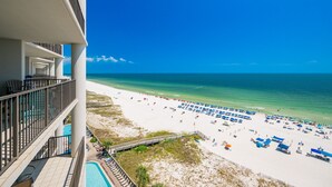 Blick auf einen Strand vom Hotelbalkon mit Pool, Liegestühlen und Sonnenschirmen.