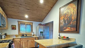Eine Küche mit Holzausstattung, einem Edelstahlkühlschrank, einer großen Kochinsel mit Barhocker und einem Bild an der Wand.