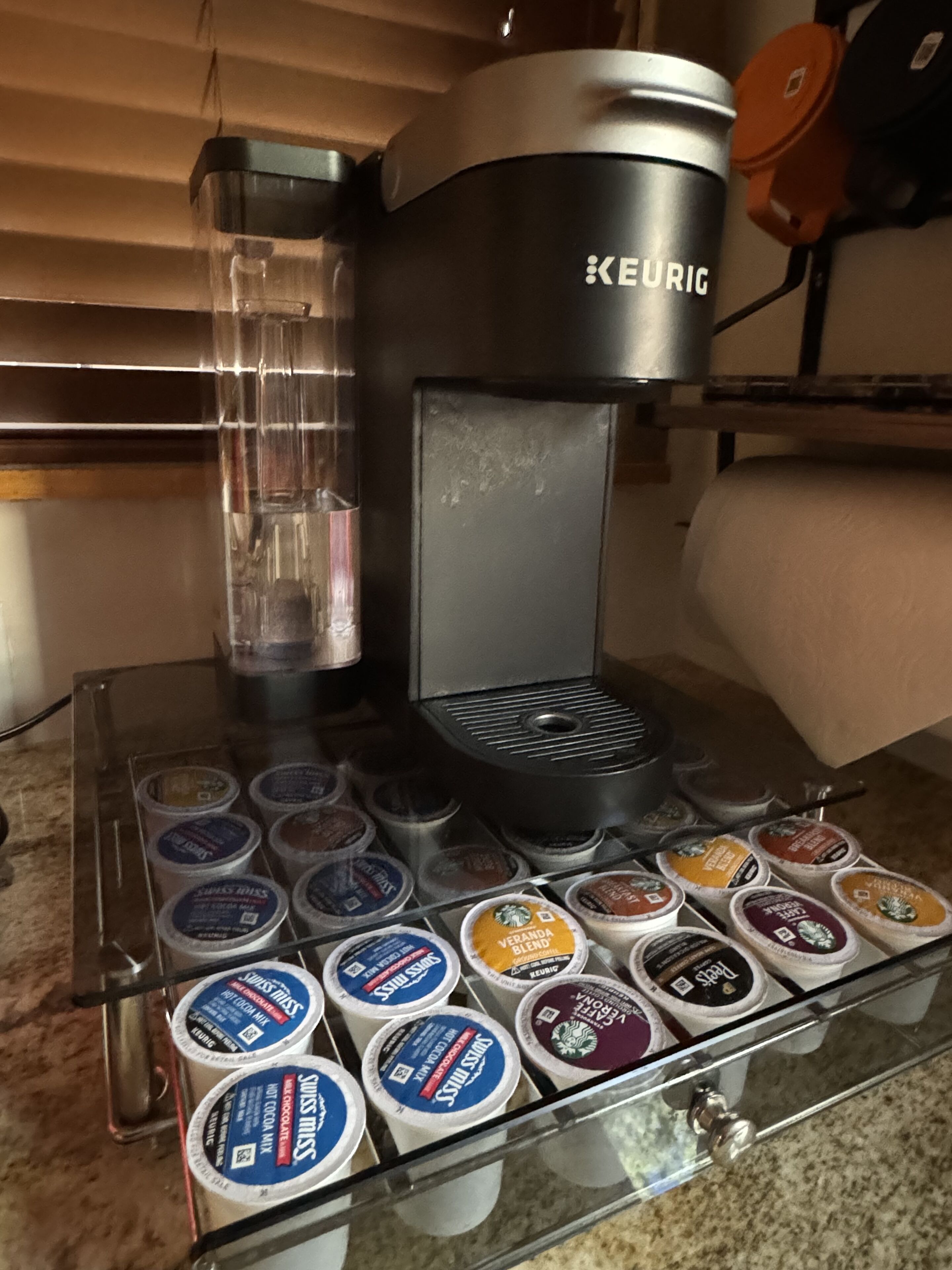 Une machine à café Keurig dotée d’une verseuse en verre et d’un bac de récupération, ainsi qu’un support pour les capsules de café, compatible avec différentes marques.