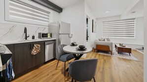 A modern kitchen with a dining area, a sofa, and a window with blinds. - Elegant|Spacious|King Bed|Fireplace|Ravine View (Edmonton)