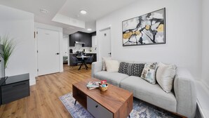 A modern living room with a grey sofa, a wooden coffee table, and a painting on the wall. - Elegant|Spacious|King Bed|Fireplace|Ravine View (Edmonton)