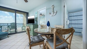 Un balcón amplio con puerta de cristal que da a una zona de piscina, una mesa redonda con sillas y un televisor sobre un mueble.