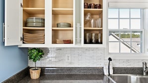 A kitchen with white cabinets, a granite countertop, a potted plant, and a view through a window.