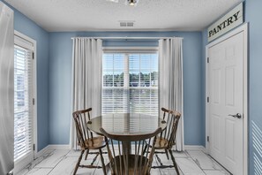 A dining area with a table and chairs, a window with curtains, and a door labeled "PANTRY".