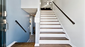 A staircase with wooden steps and a black handrail, leading to a room with a ceiling fan.