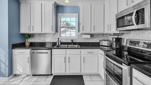 A modern kitchen with white cabinets, a black countertop, stainless steel appliances, and a window with a view of the outside.