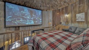 Ein Zimmer mit einer großen Anzeige, die eine Unterwasserlandschaft zeigt, Holzwänden, einer karierten Bettdecke und einem rustikalen Deckenventilator.