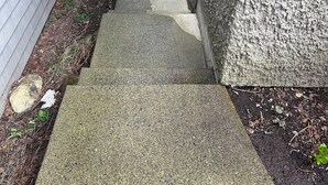 A narrow concrete pathway leading to a wooden gate, flanked by a grey house and a textured wall. - Private Garden Suite Close to UBC, Airport & Downtown (Vancouver)