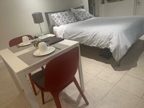 Une chambre d’hôtel avec un lit, une table et une chaise, une lampe et une table de chevet avec une tasse et une soucoupe.