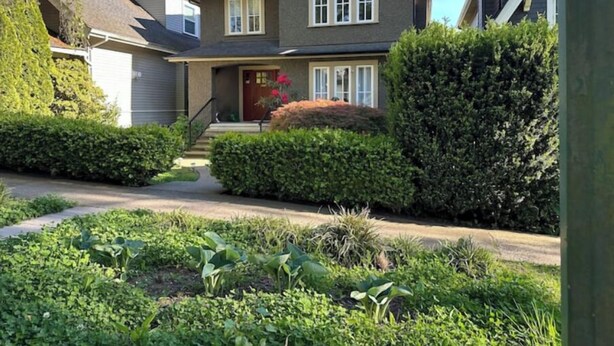 A two-story house with a front porch, a garage, and a well-maintained garden. - Private Garden Suite Close to UBC, Airport & Downtown (Vancouver)