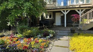 A two-story building with a covered patio area, outdoor seating, and a variety of colorful flowers in the garden. - Private Garden Suite Close to UBC, Airport & Downtown (Vancouver)