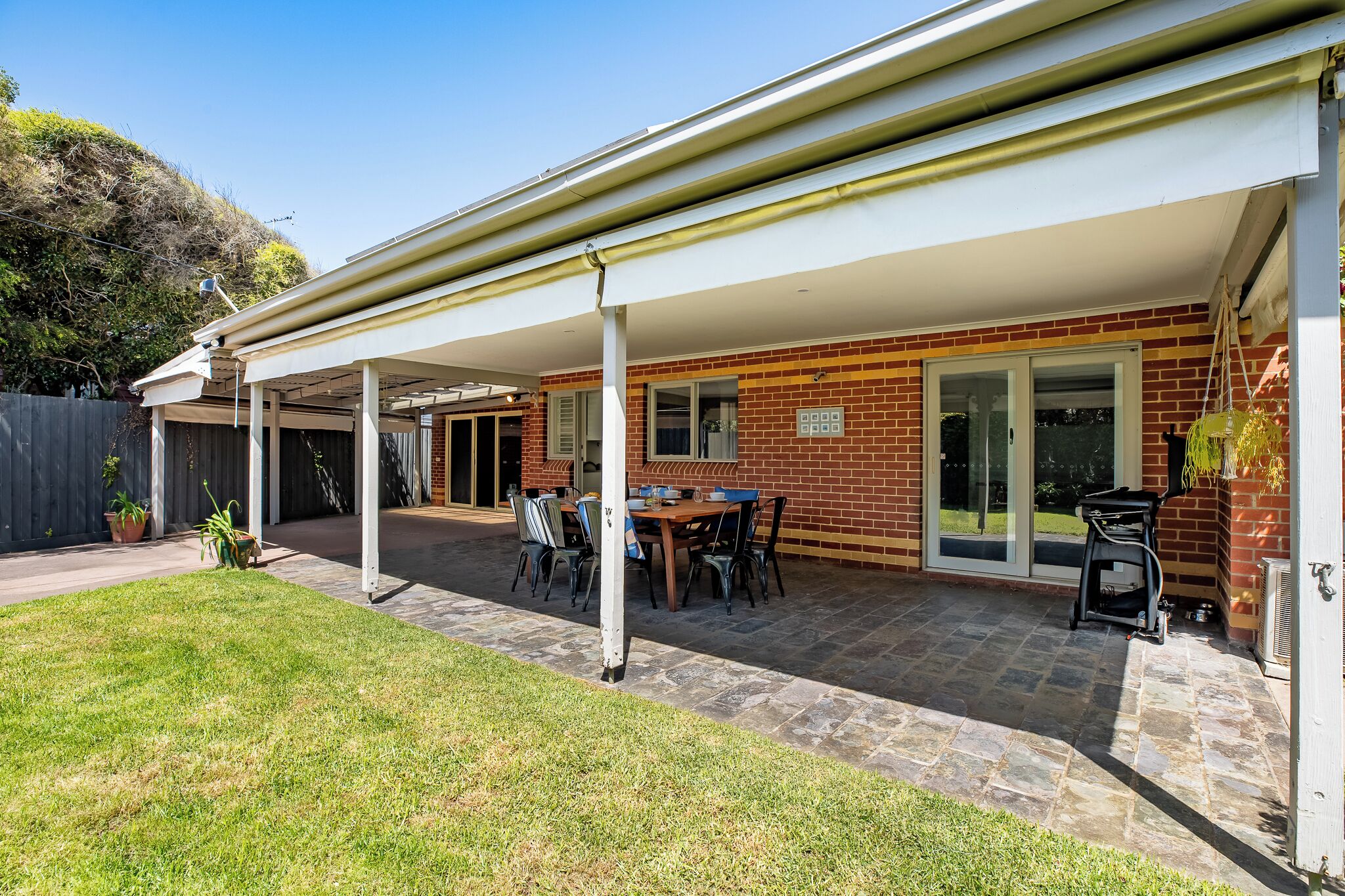 A covered patio with a brick exterior, a table and chairs, and a grill area.