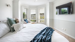 A bedroom with a bed, a ceiling fan, a TV mounted on the wall, and a window with blinds. - Spacious | Pet Friendly | Ping Pong Table | Near Beach (Ocean Grove)
