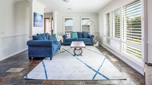A spacious living room with two blue sofas, a coffee table, and a large window with blinds. - Spacious | Pet Friendly | Ping Pong Table | Near Beach (Ocean Grove)