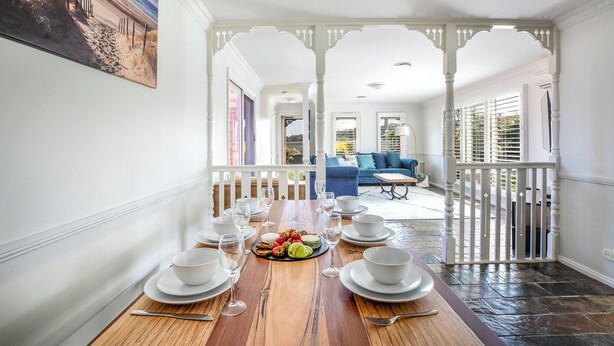 A dining area with a wooden table set for six, white plates, and a fruit platter. - Spacious | Pet Friendly | Ping Pong Table | Near Beach (Ocean Grove)