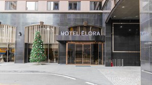 A modern hotel entrance with a large glass door, a Christmas tree, and a sign reading "HOTEL ELORA".