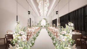 A spacious hall with a central aisle leading to a floral arch, surrounded by tables and chairs.