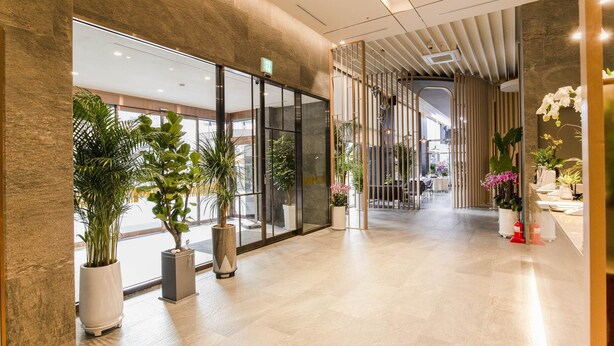 A spacious lobby with a modern design, featuring a glass wall, potted plants, and a wooden partition.