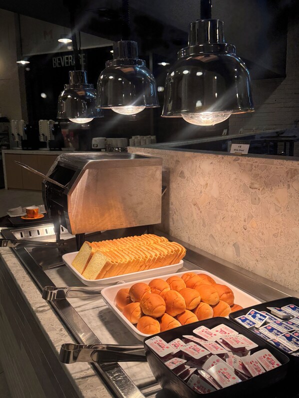 A buffet counter with bread, buns, and packaged food items.