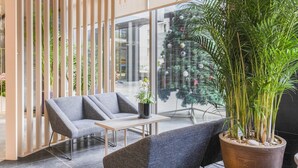 A modern indoor space with a seating area featuring two grey sofas, a small table, and a large potted plant.