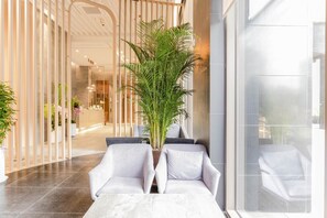 A modern lobby with a reception desk, white chairs, a large potted plant, and a glass wall. - HOTEL ELORA (Yongin)
